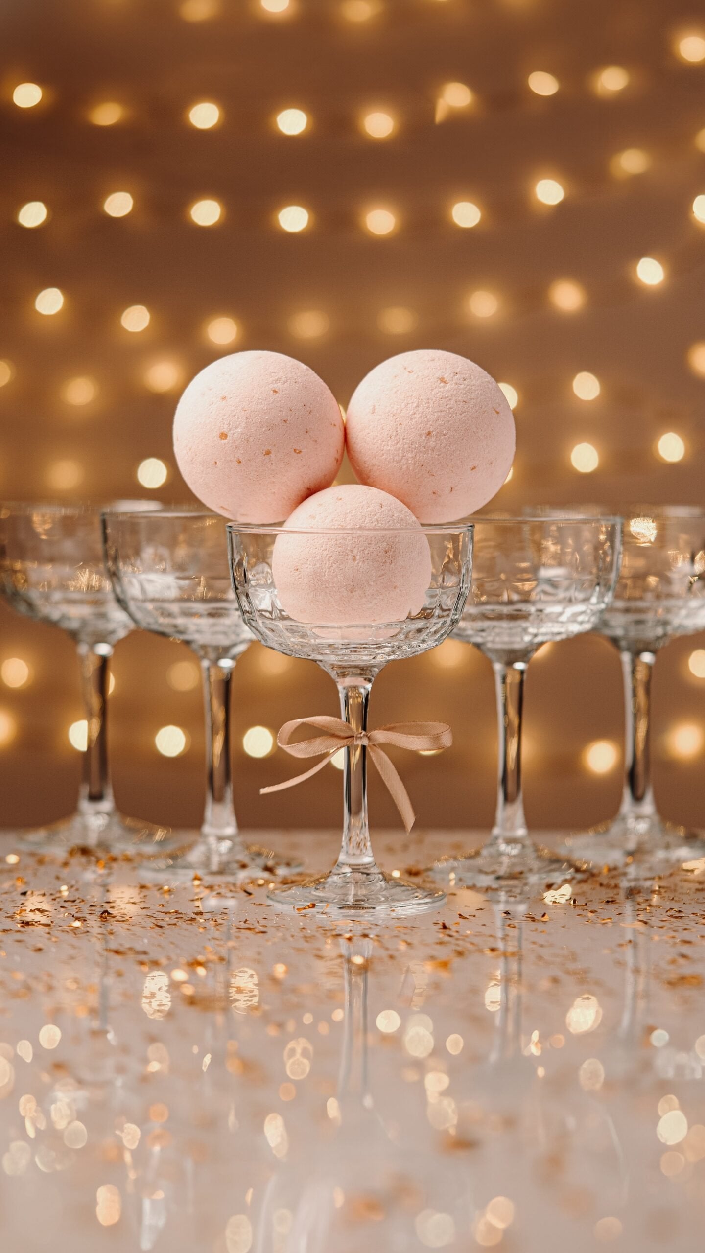 Bath bombs in champagne glasses against a backdrop of festive lights