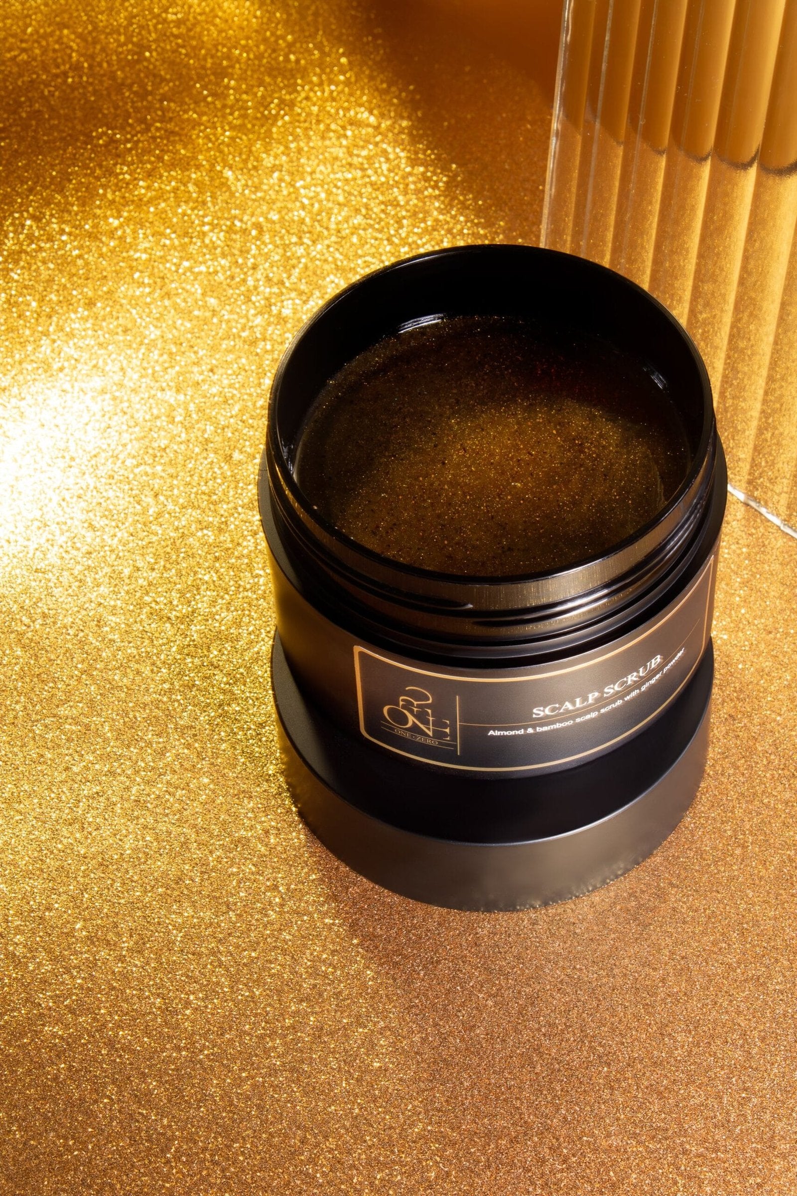 A jar of scalp scrub on a golden shimmering surface