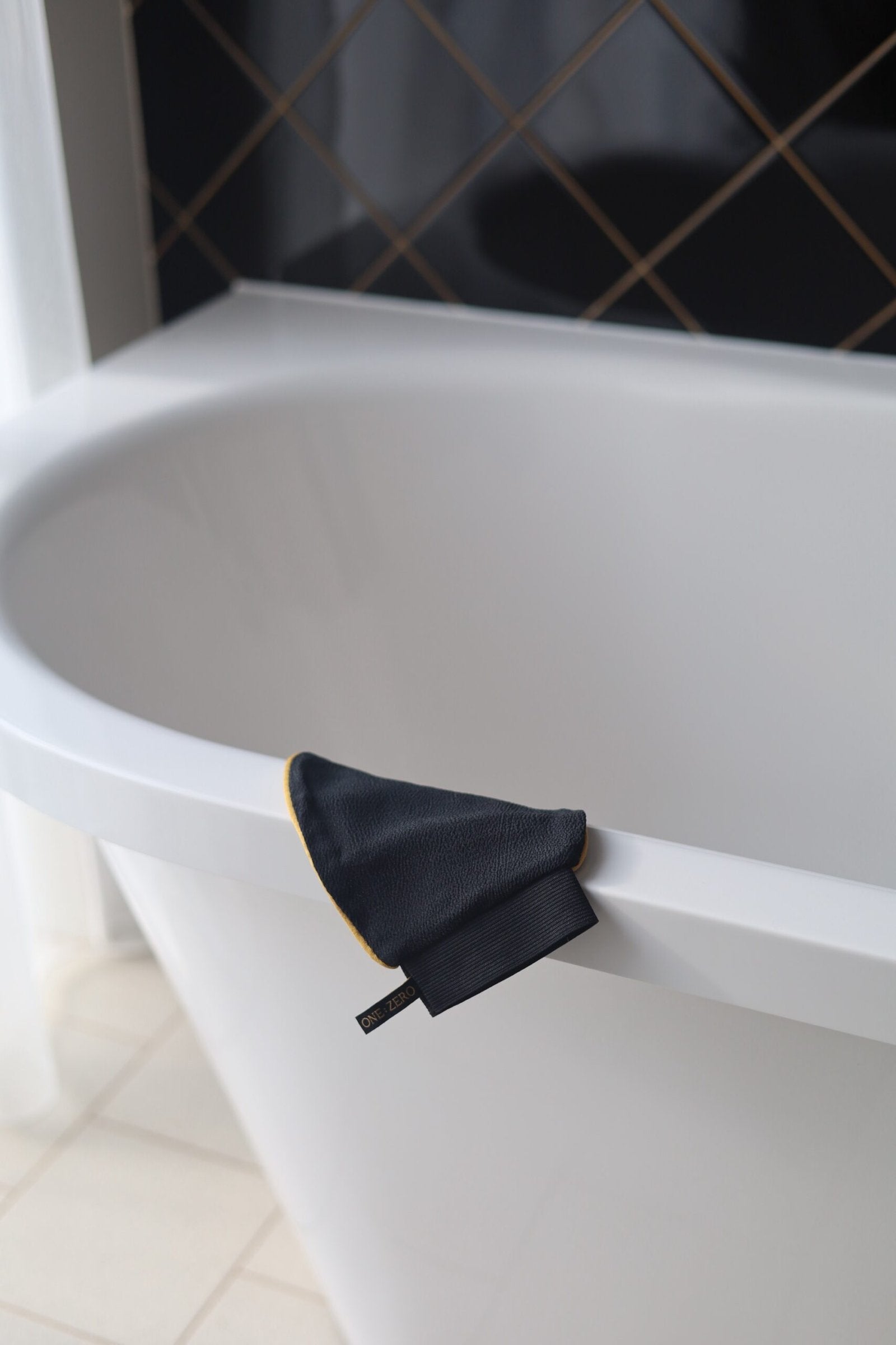 A black scrub glove on the edge of a white bathtub